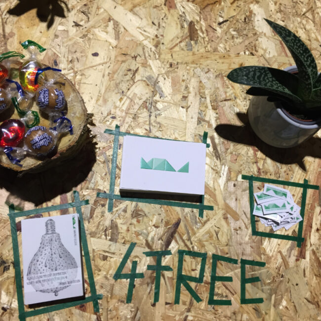 Pressspanplatte des selbstgebauten Messestands von MOLD mit Visitenkarten, Stickern, einer Sukkulente, einer Holzscheibe und Bonbons — das Wort „4 FREE“ mit Maskingtape gestaltet